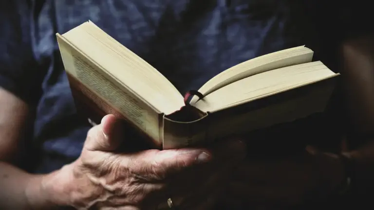 A pair of hands holding an open book with pages fanned, in a dimly lit setting