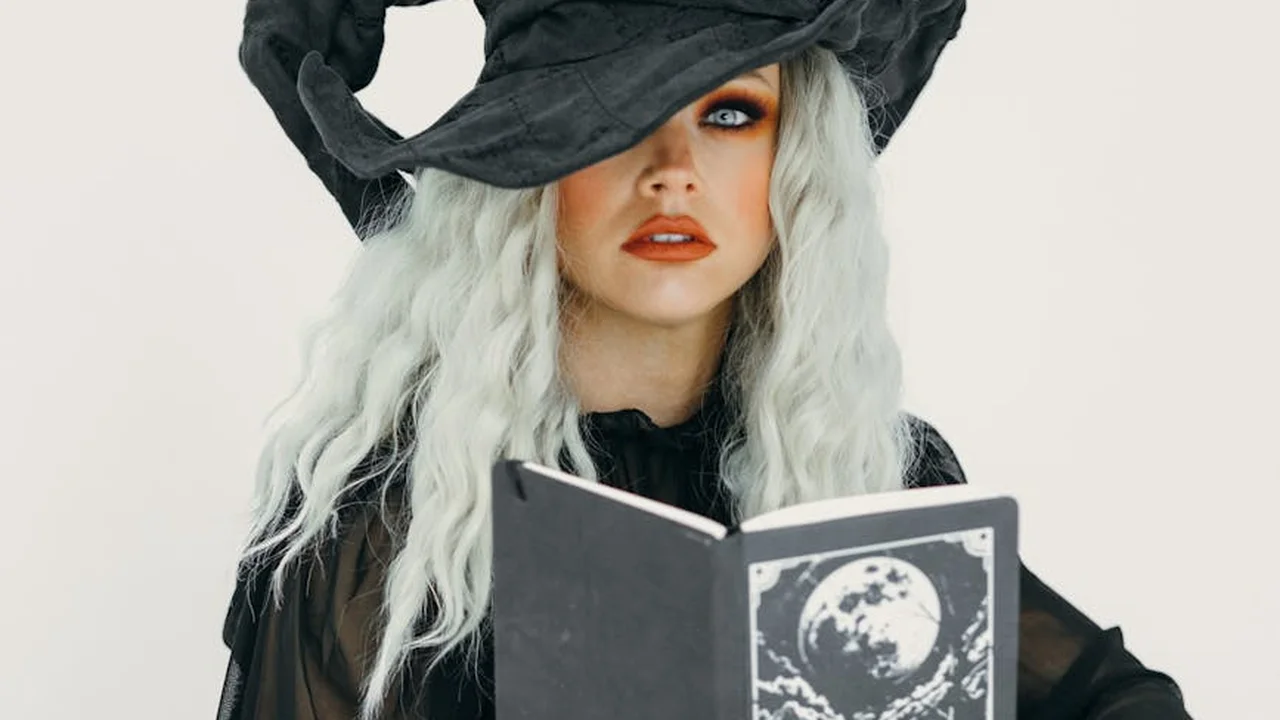 Person wearing a black witch hat and cape, reading a book