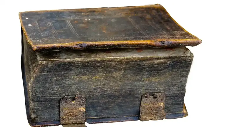 A large, heavy leather-bound book with a dark, worn cover and rusted metal clasps, set against a white background.
