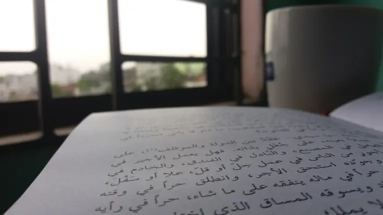 Close-up of a notebook with Arabic handwriting on a desk by a window, symbolizing learning from diverse voices