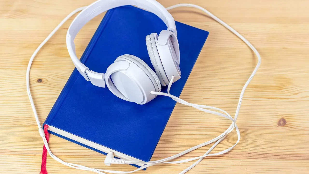 White over-ear headphones resting on a blue hardcover book on a wooden table