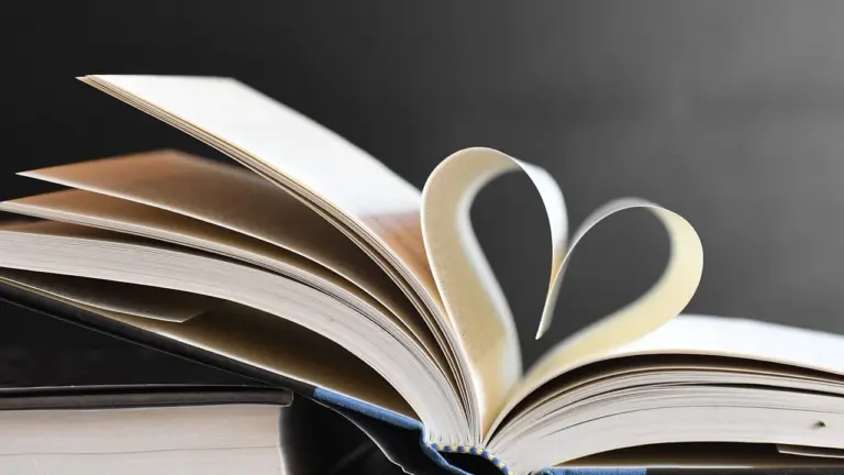 An open book with pages curved to form a heart shape against a dark background.