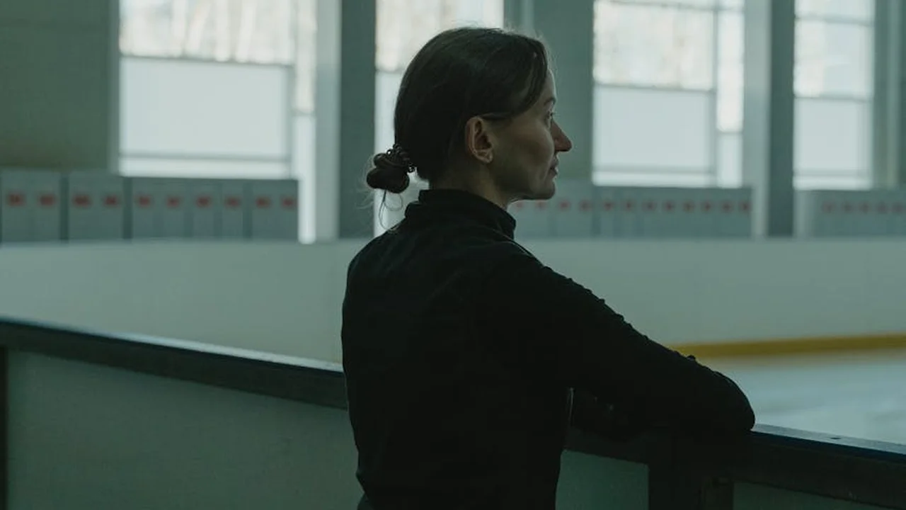 Female hockey player at rink boards, looking away with a focused expression.