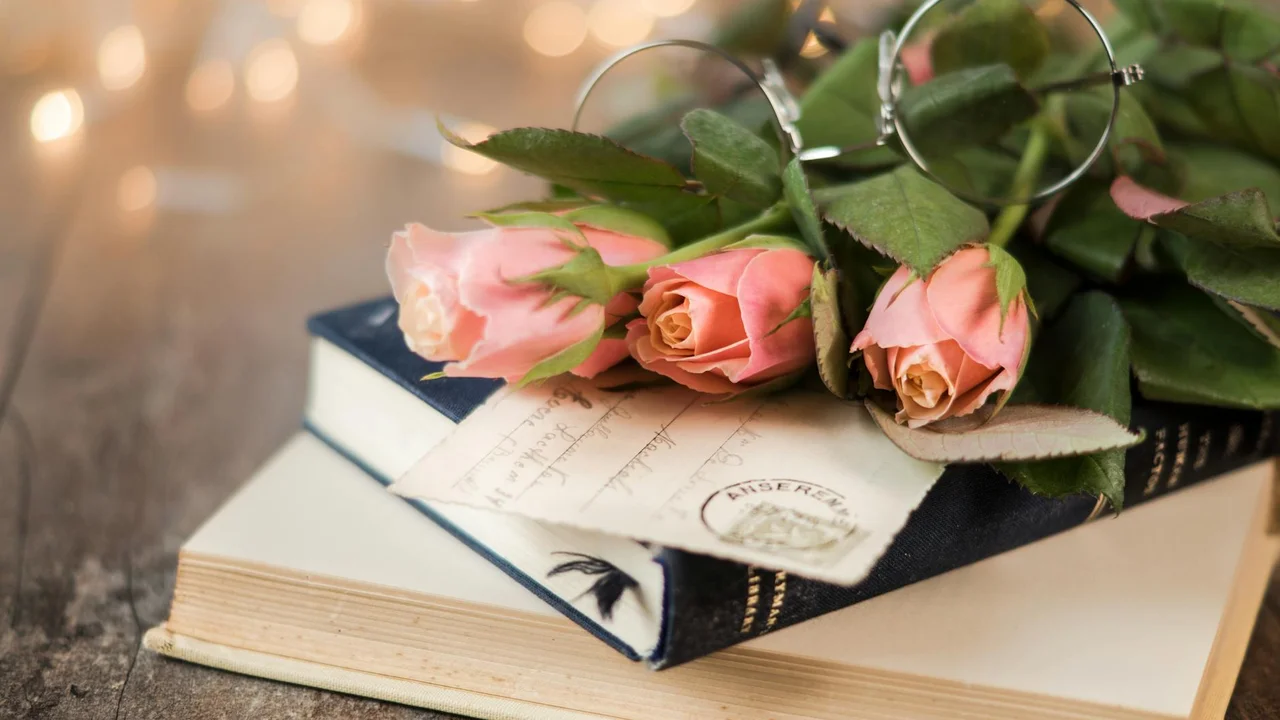 Pink roses on top of a stack of books with a pair of reading glasses