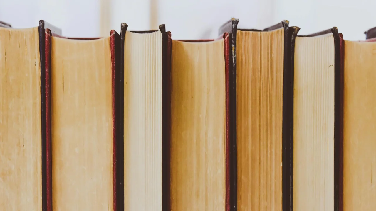 Row of old hardback books with beige to brown spines on a shelf.
