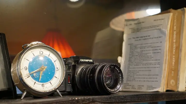 Vintage camera, blue-faced alarm clock, and stacked books on a shelf.