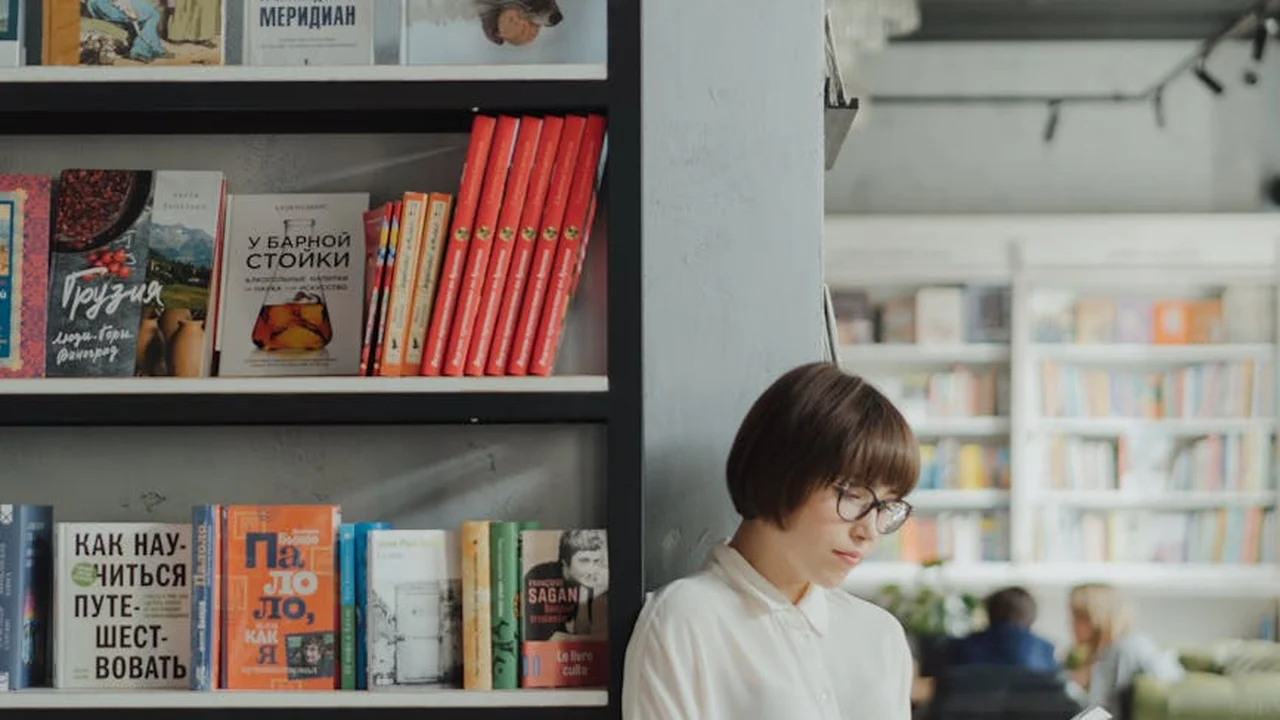 Person wearing glasses browsing colorful books on a shelf in a bright bookstore