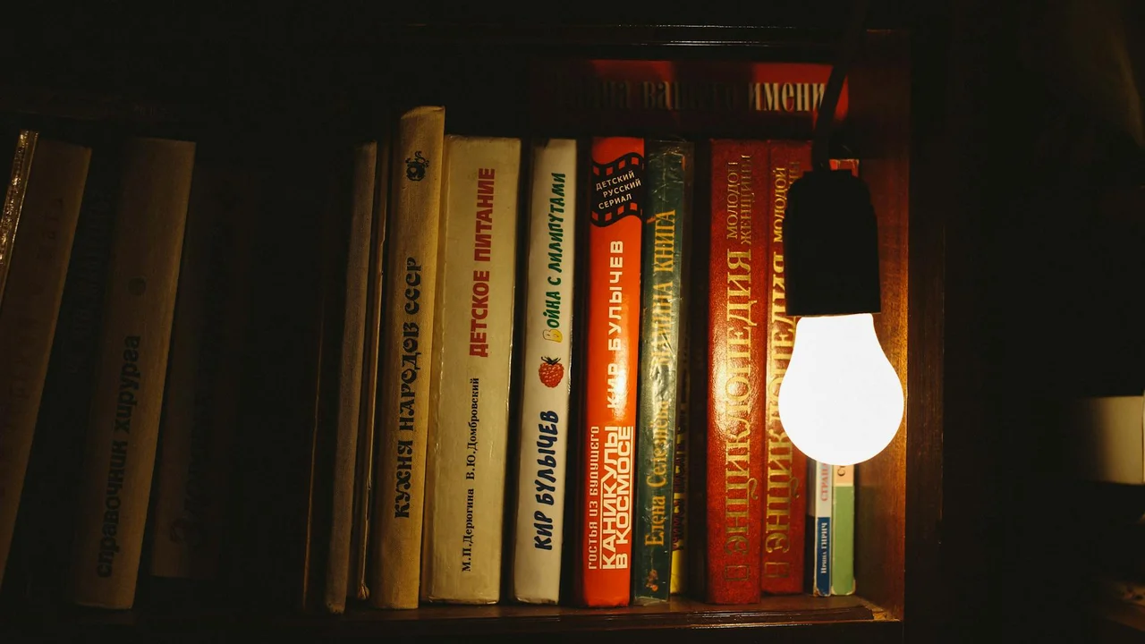 A dimly lit bookshelf filled with magical and occult novels, with a single hanging light bulb casting warm glow on the spines.