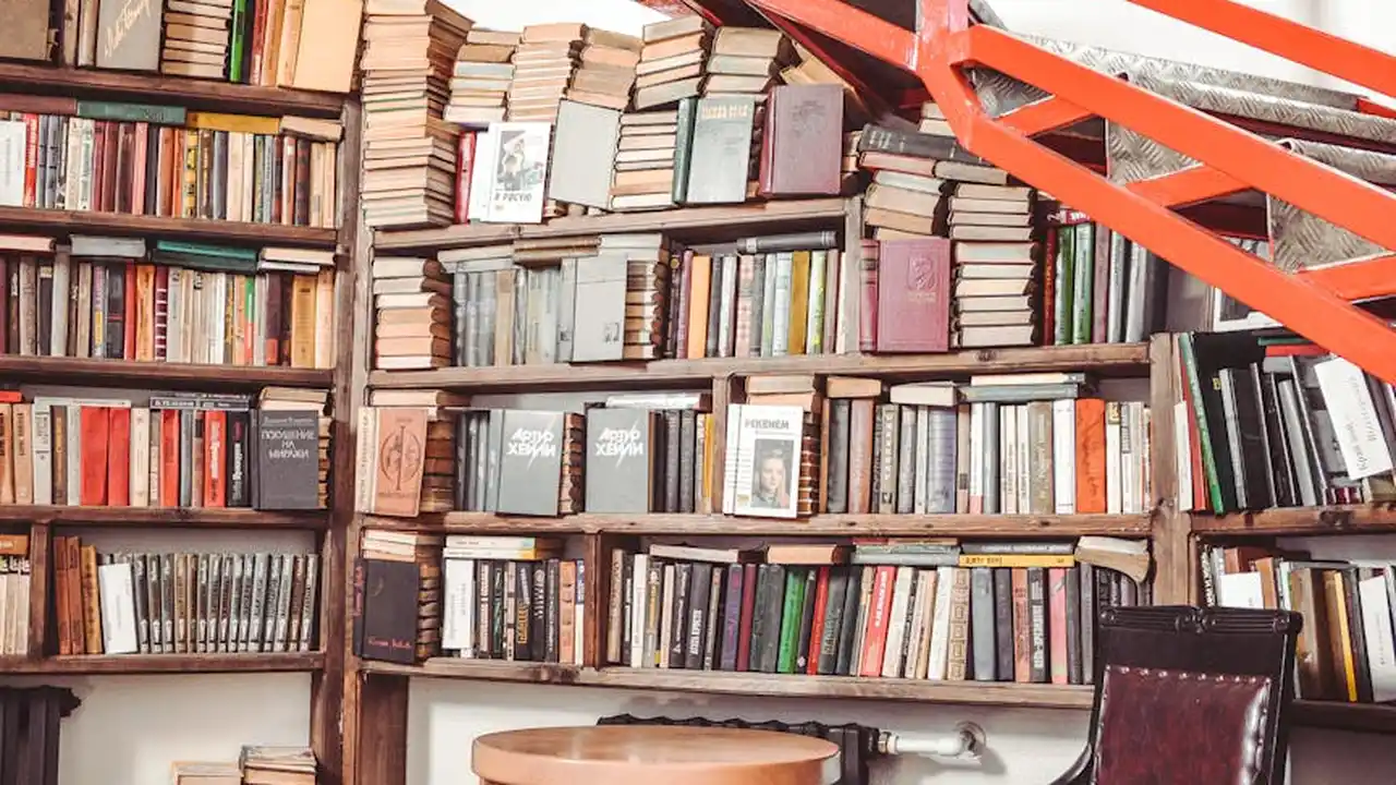 A dense library with floor-to-ceiling shelves filled with books and a red metal staircase cutting across the upper right corner