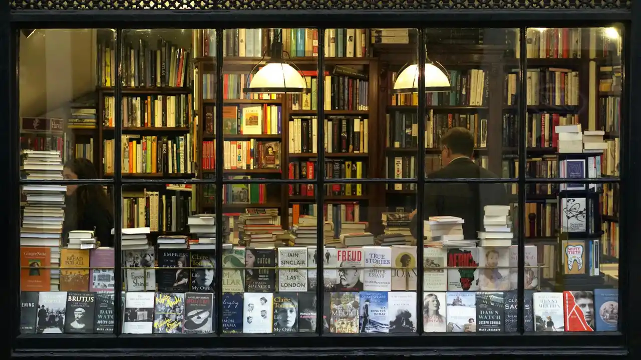 Inside a bookstore window with shelves of books and two people browsing the collection