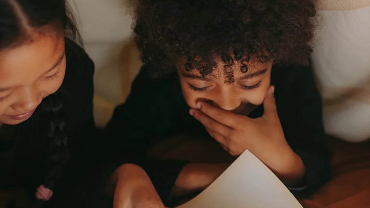 Two children indoors, leaning over a sheet of paper as they read or discuss together.