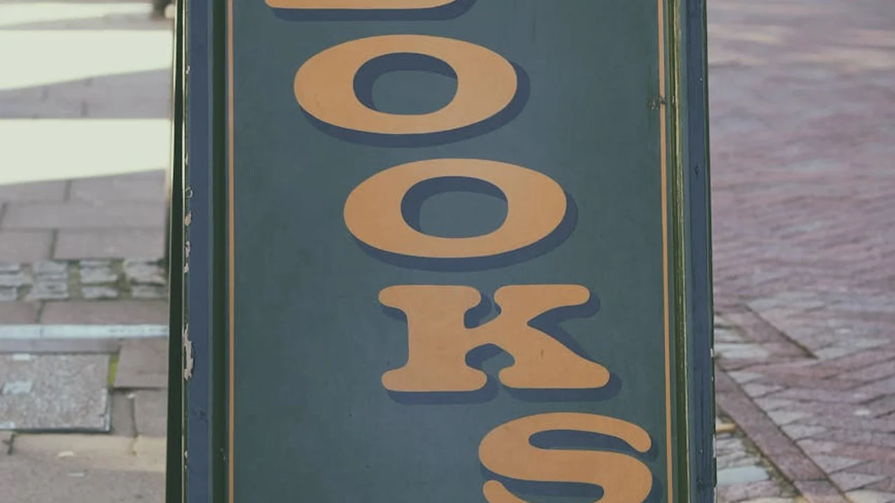 Vertical blue sign with orange letters reading 'COOKS' arranged top to bottom, adjacent to a sidewalk.