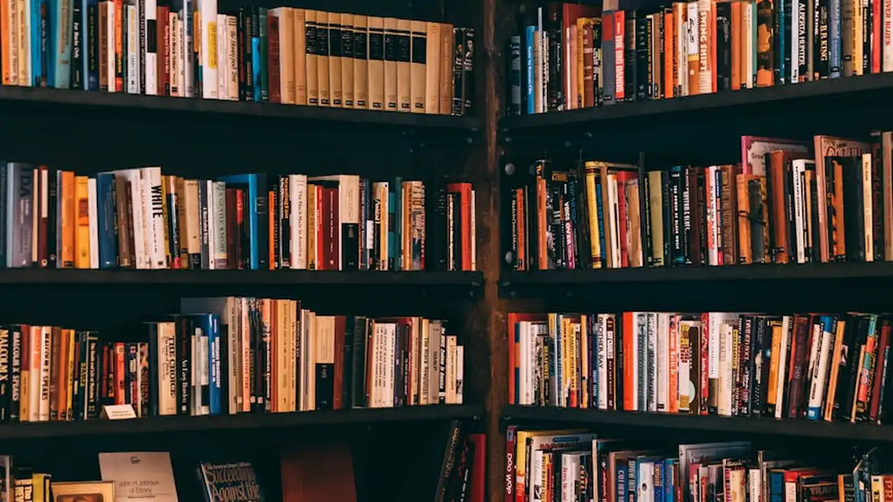 Rows of warm-colored books on tall wooden shelves in a cozy library or bookstore, suggesting a community-driven reading space.