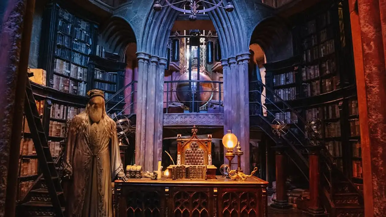 Gothic library with towering shelves, a robed figure near a carved desk, warm lamp glow and blue-toned lighting creating a moody dark fantasy atmosphere.