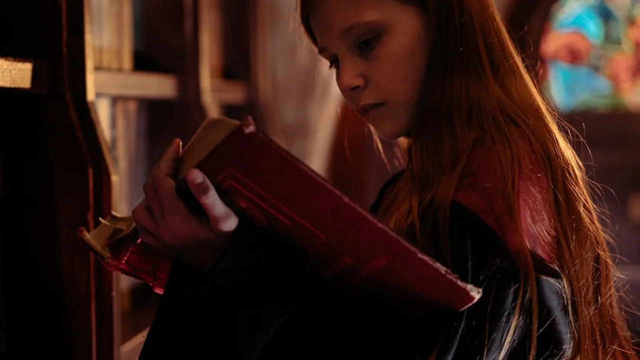 Young woman reading a red-covered book in a dimly lit, moody library setting