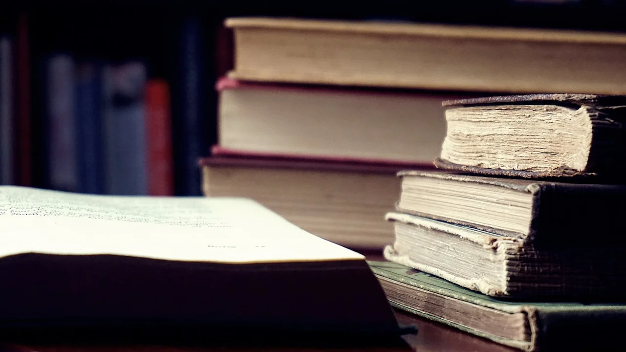 Open book resting on a stack of worn hardcover books in a warm-lit library, evoking late-night reading and dreamlike atmospheres.