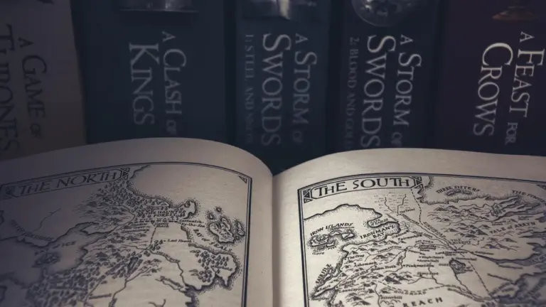 Open fantasy book showing a detailed map; the scene is set on a shelf with the spines of fantasy novels, including A Game of Thrones, visible in the background.
