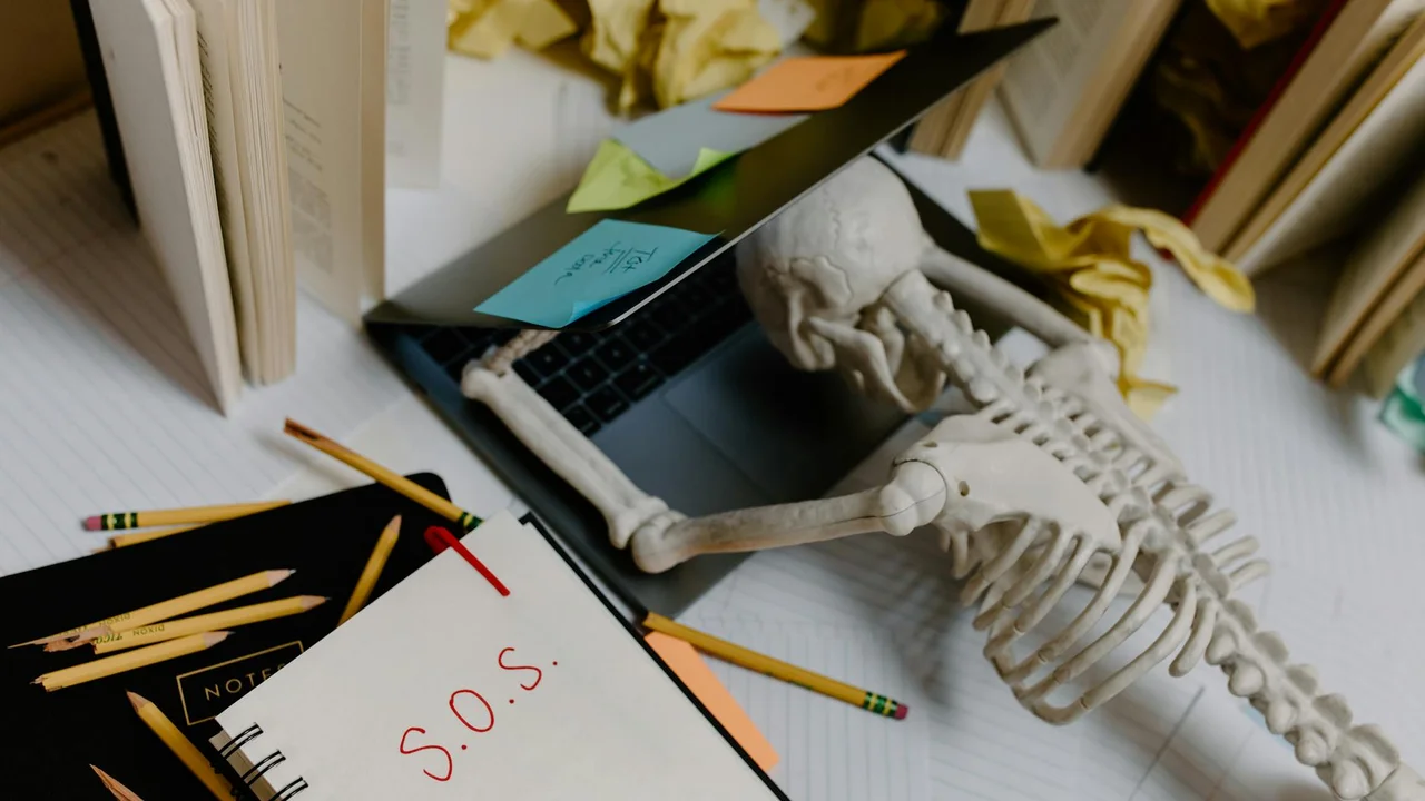 A desk scene featuring a small skeleton model among sticky notes, pencils, and an open notebook, suggesting study of science and history related to pandemics.
