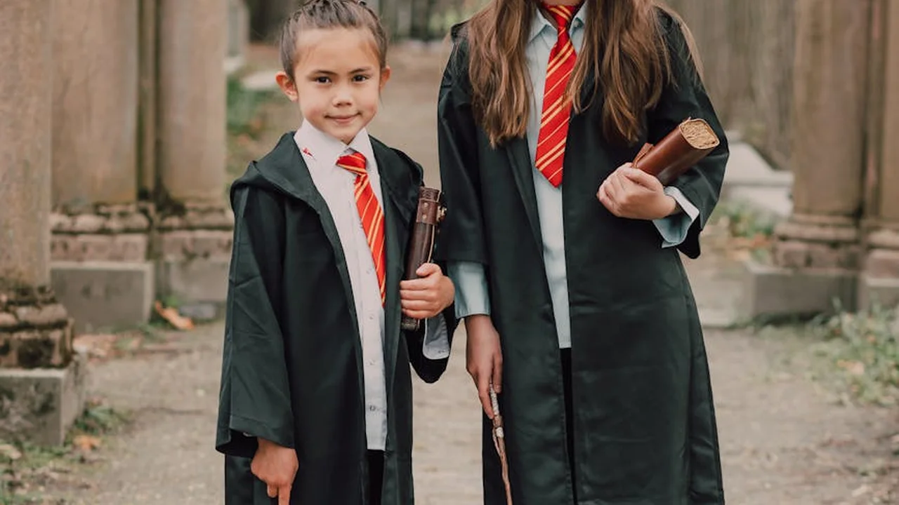 Two young students in dark wizard robes with red-and-gold striped ties, each holding a wand, standing in a stone archway.