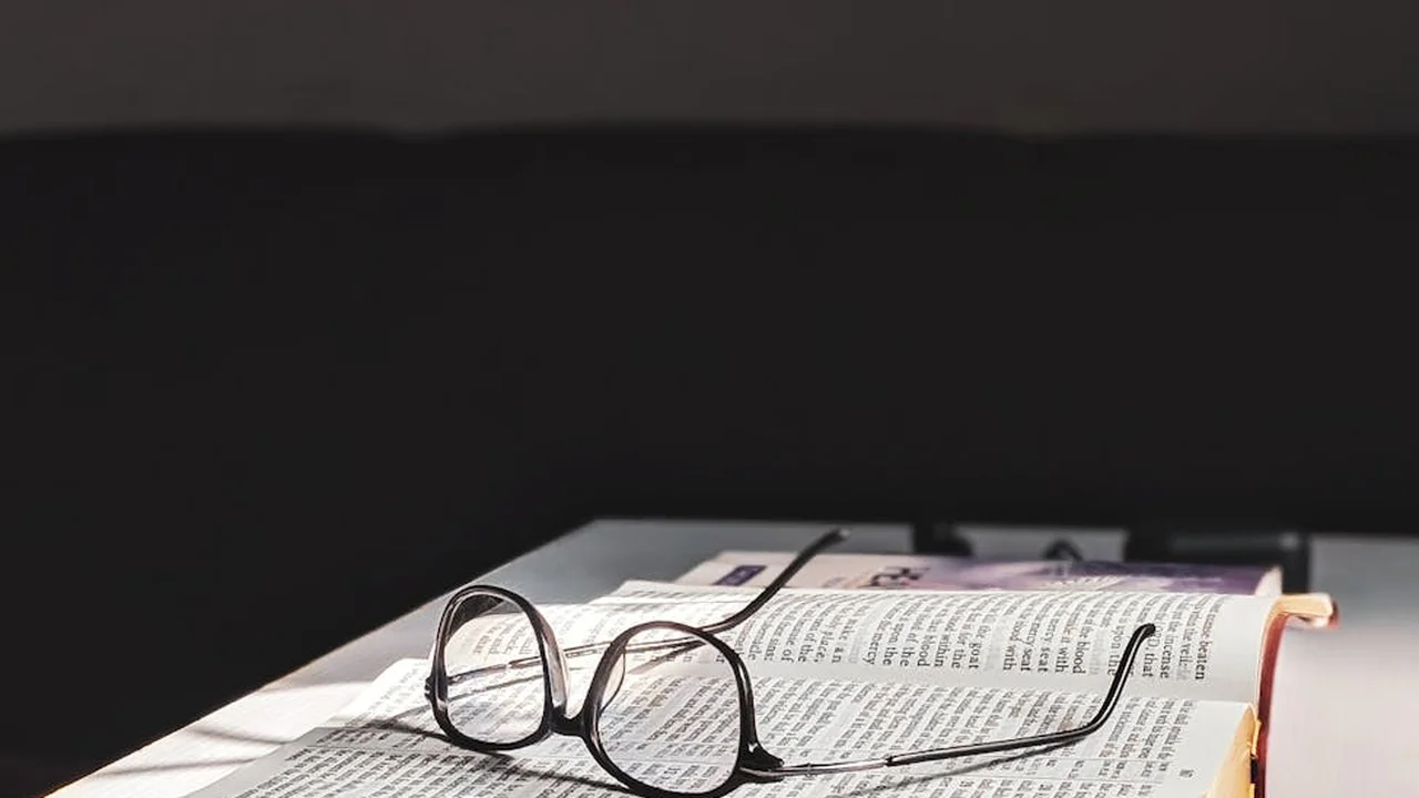 Round eyeglasses resting on an open book with dense text.