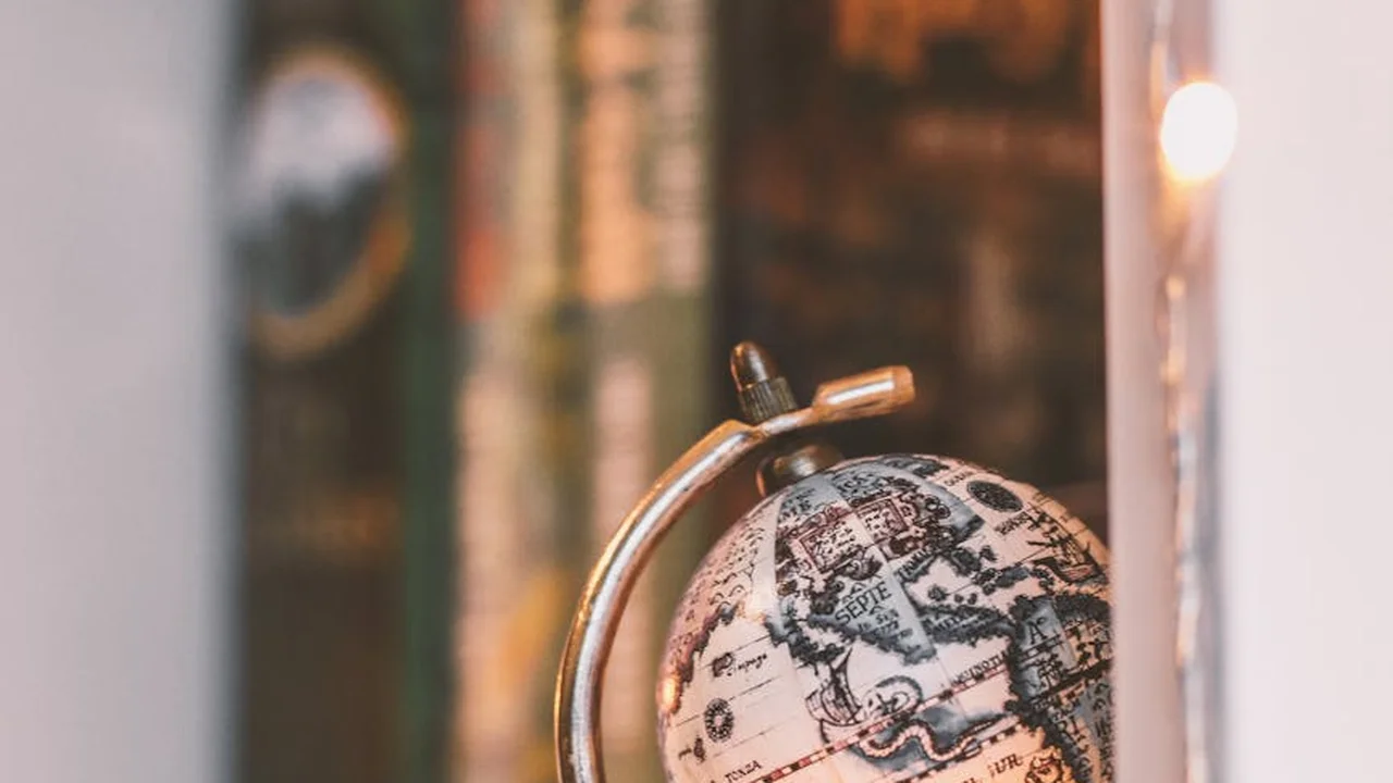 A vintage globe sits on a desk with a softly blurred bookshelf in the background, evoking travel and storytelling.