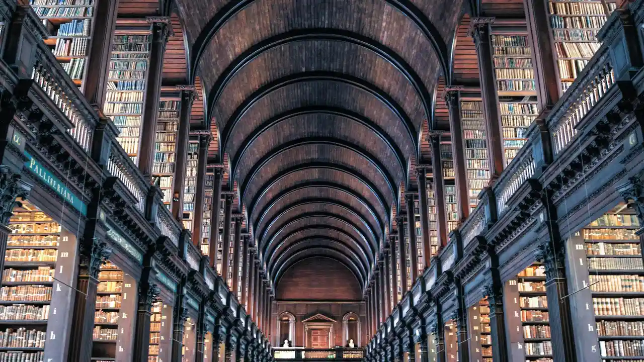 Interior of a grand gothic library with vaulted wooden ceilings and tall book-filled shelves bathed in warm amber light.