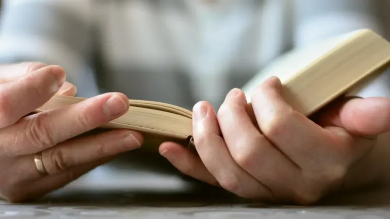 Close-up of hands holding a small open book, symbolizing study, devotion, and spiritual reflection