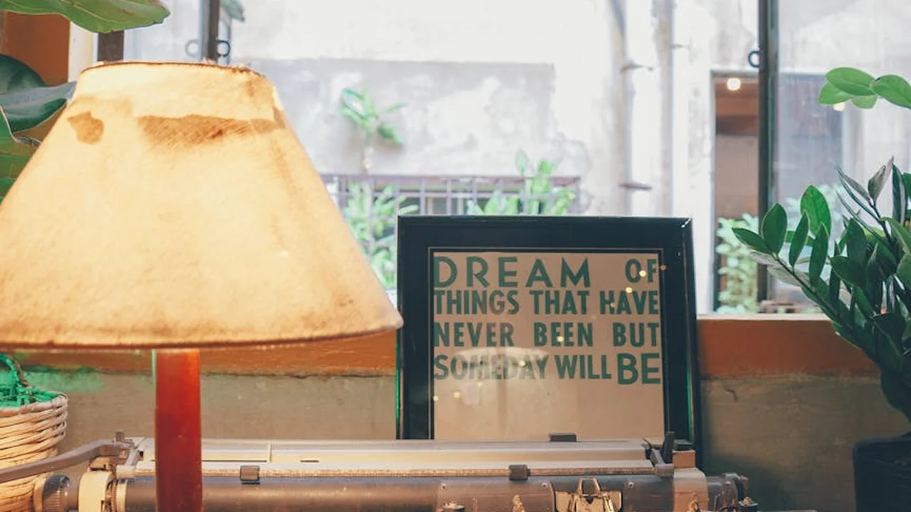 Cozy desk scene with a warm yellow lamp, green plants, and a framed quote about dreams and possibilities.