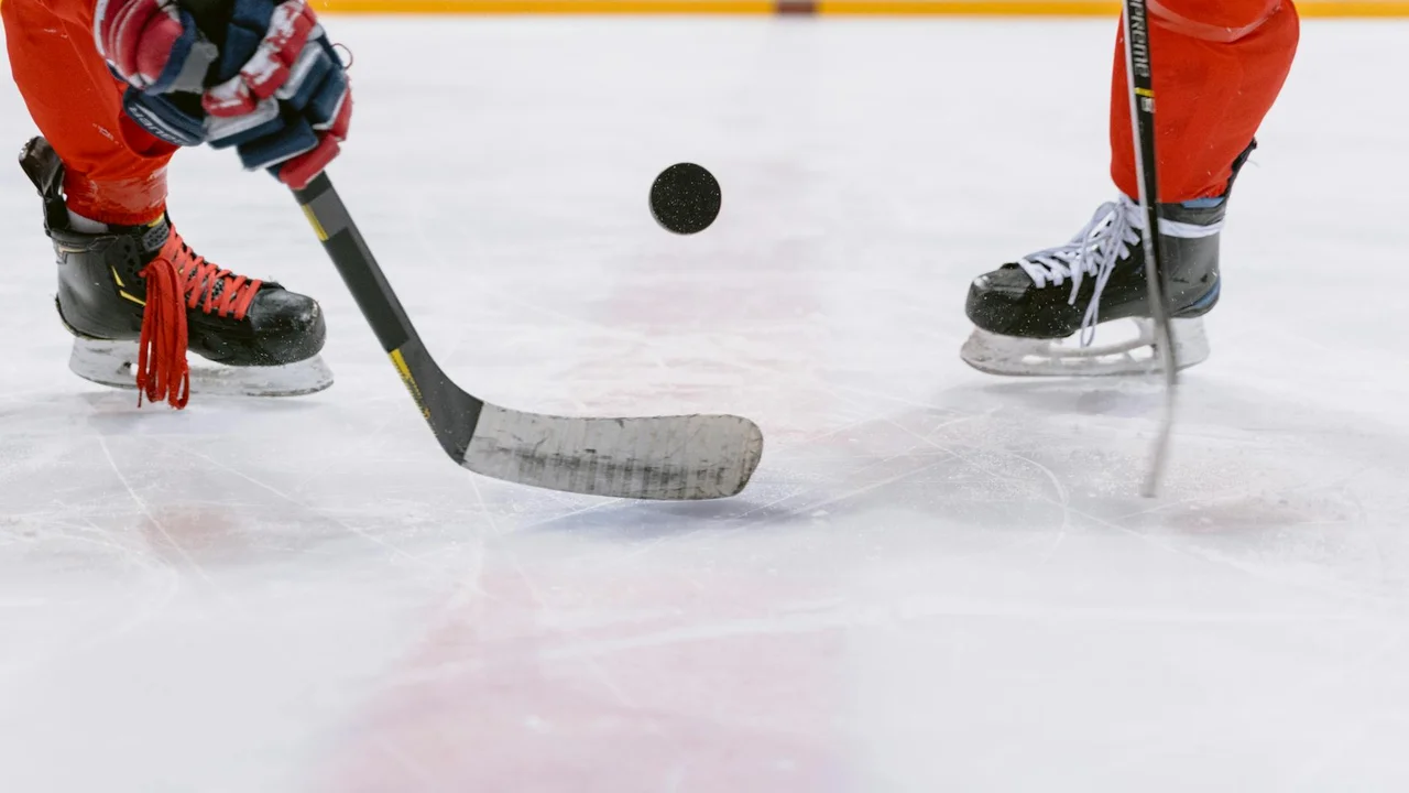 Two hockey players facing off on an ice rink with a puck suspended between their sticks