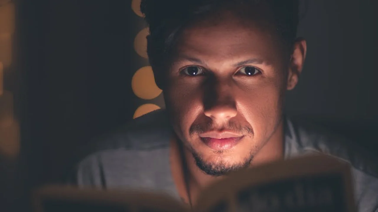 Close-up of a person reading a book in a dimly lit setting, with a focused expression.