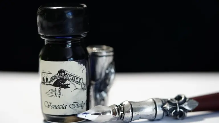 Close-up of a vintage ink bottle with a nib pen on a dark surface, evoking writing and modern, emotional poetry.