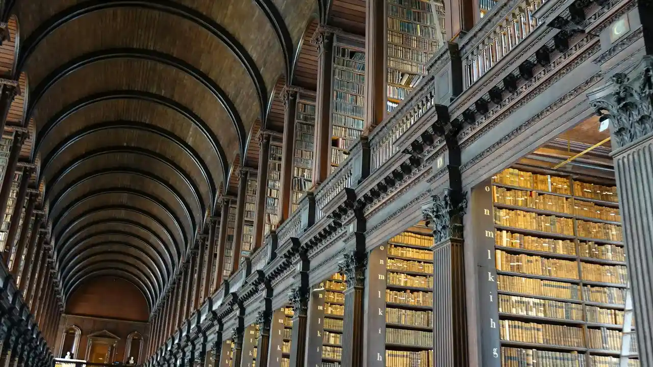 Interior of a grand library with an arched ceiling, ornate columns, and long rows of towering bookshelves filled with books.