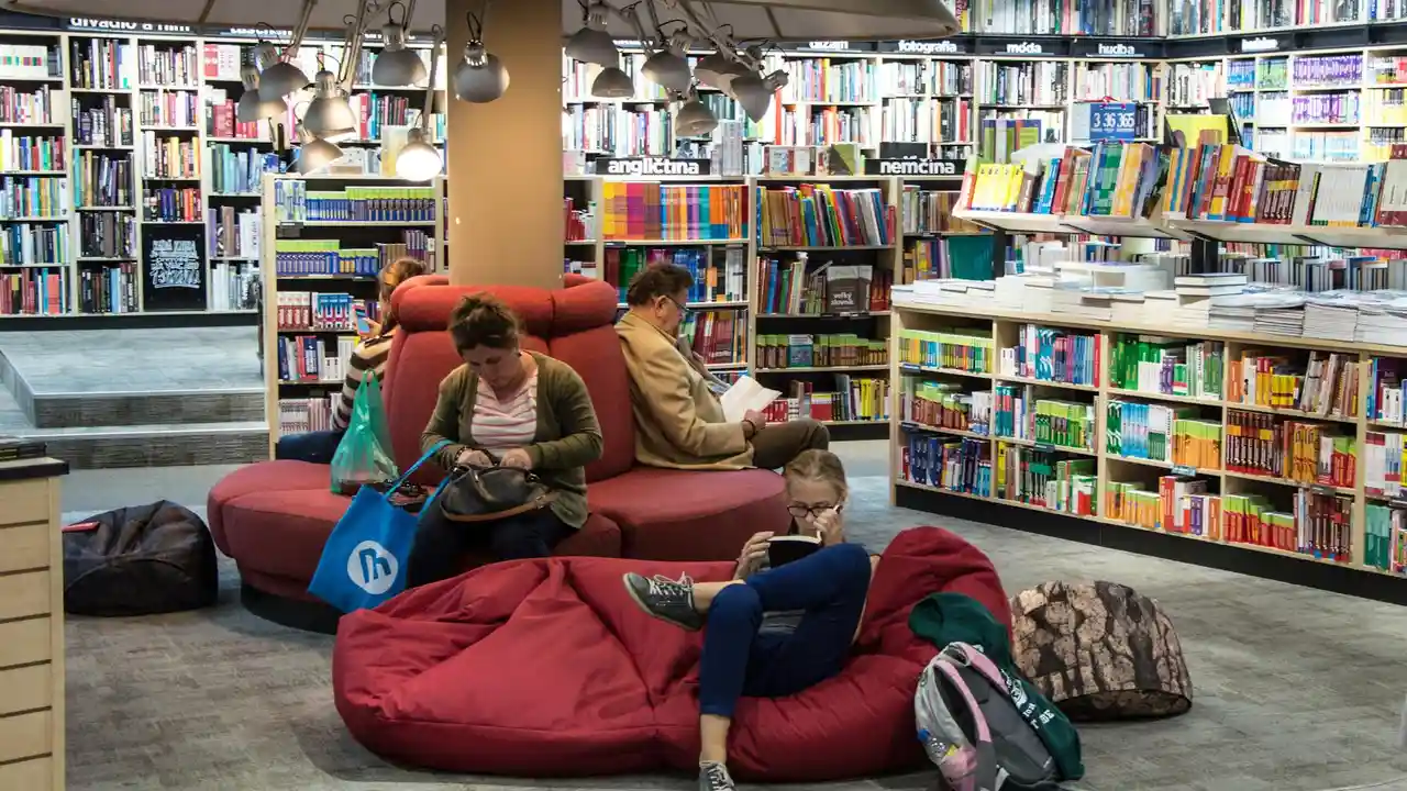 People reading on red bean bag chairs in a bright bookstore surrounded by tall shelves filled with colorful books.