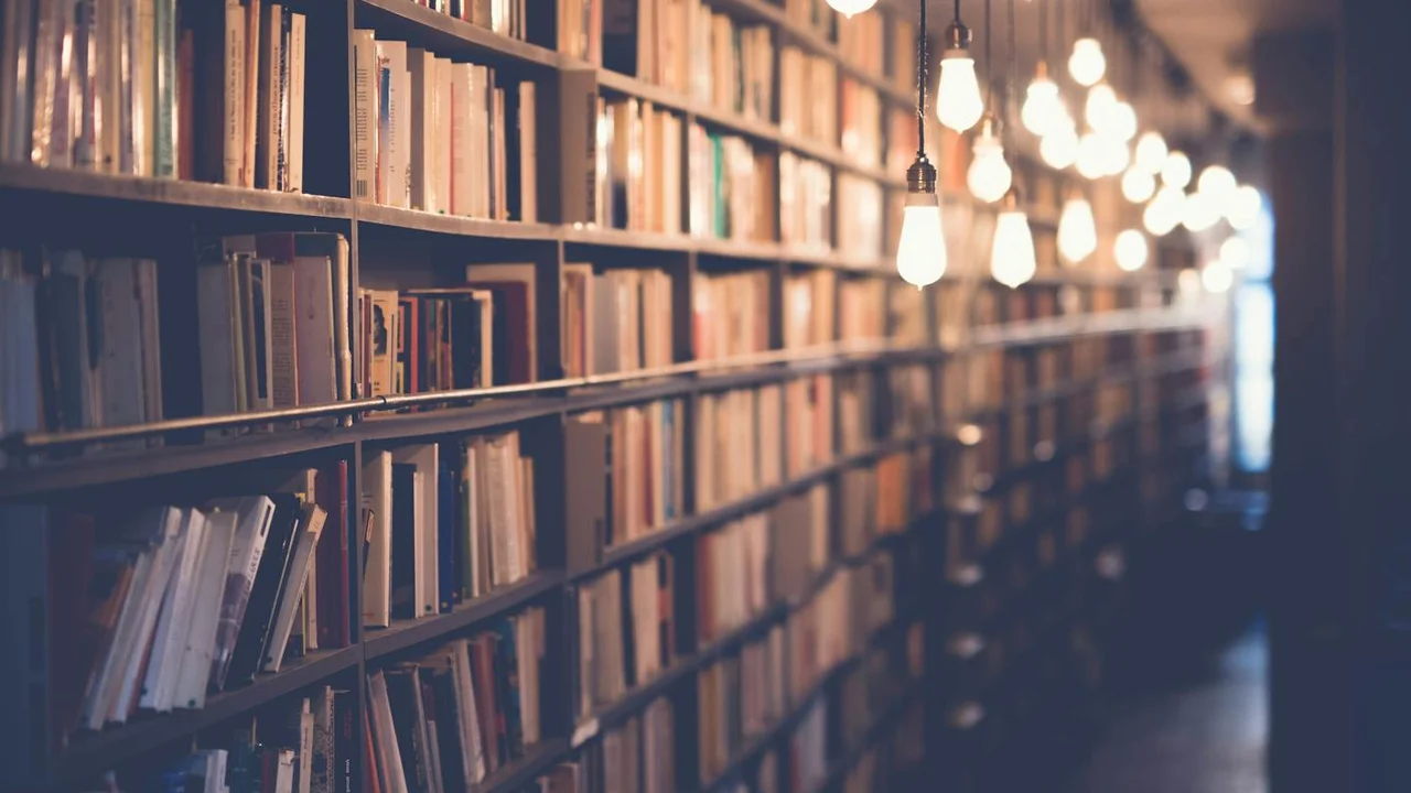 A warm library scene with tall shelves packed with books and hanging pendant lights creating soft bokeh in the background.