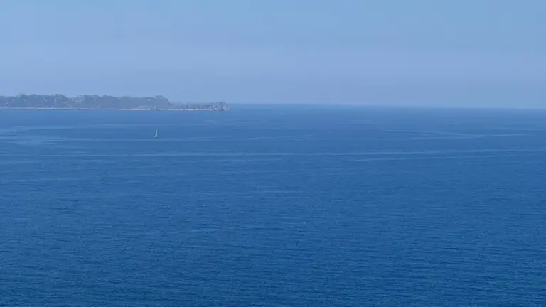 A vast blue sea with a distant coastline and a small sailboat on the horizon.