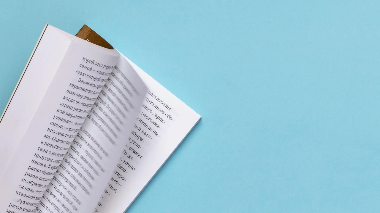Open paperback on a bright blue background with pages slightly fanned and a brown bookmark peeking out.