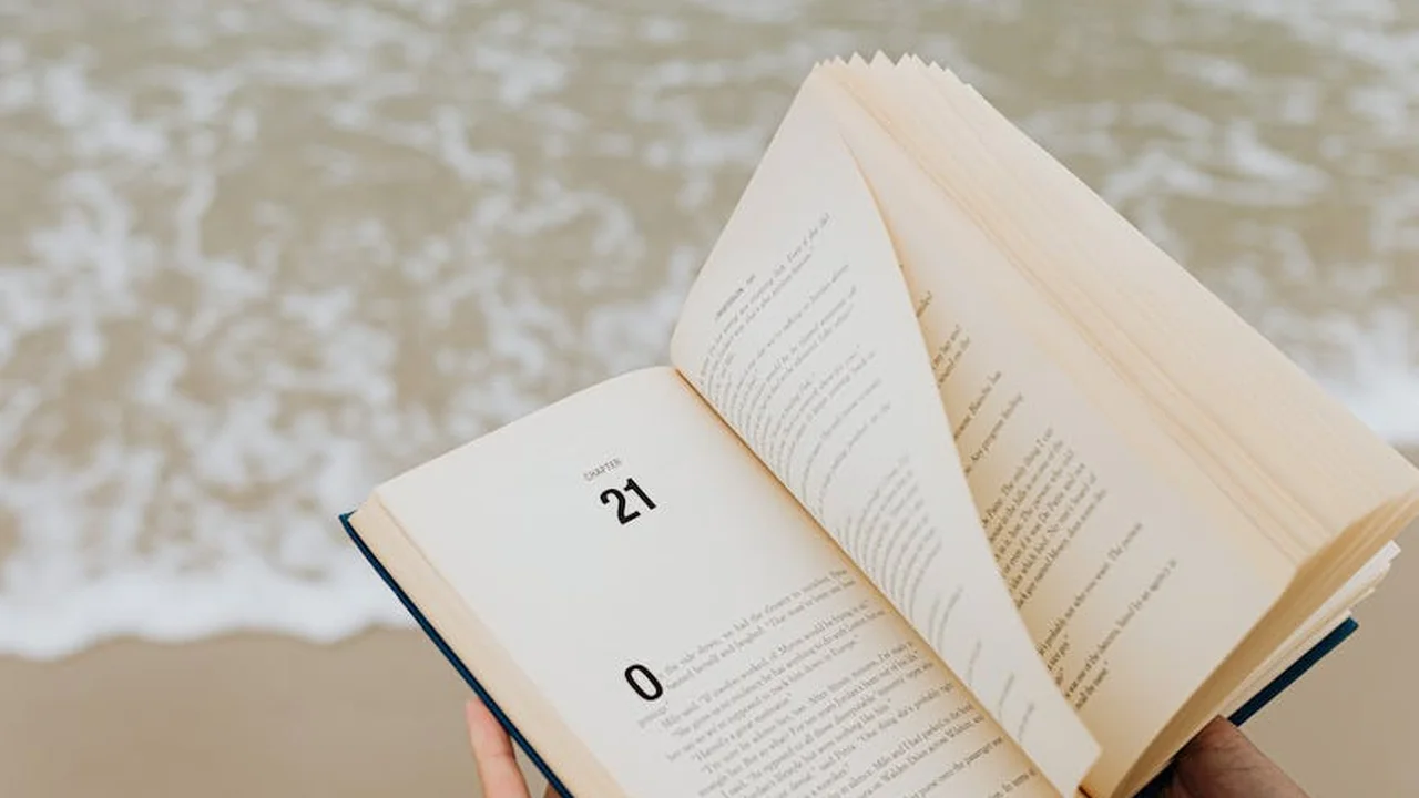 An open book resting on a sandy surface, pages slightly curled, with the numbers 21 and 0 visible on the left page.