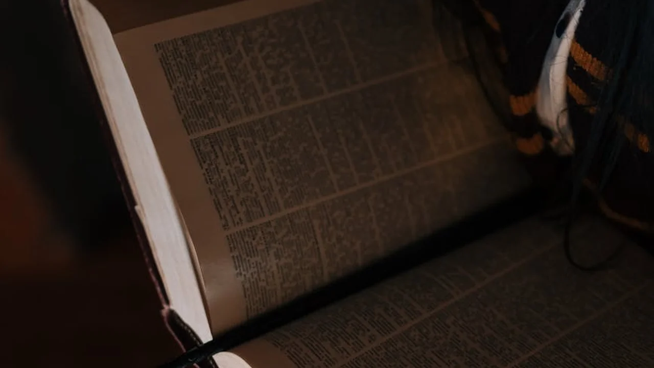 Open book with dense text spread across pages in a dimly lit setting.