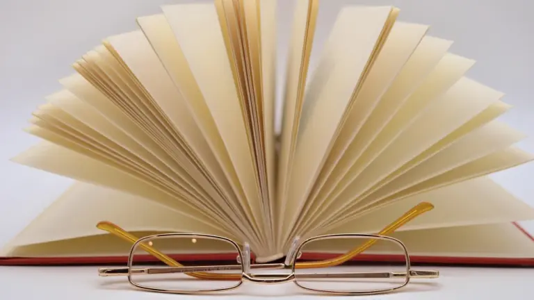 An open book with all its pages fanned out and a pair of reading glasses resting on the pages