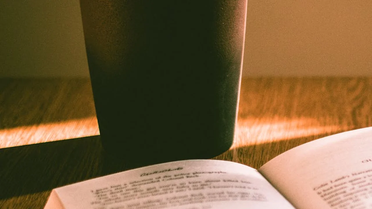 Close-up of an open book on a wooden surface with a dark mug casting a shadow.