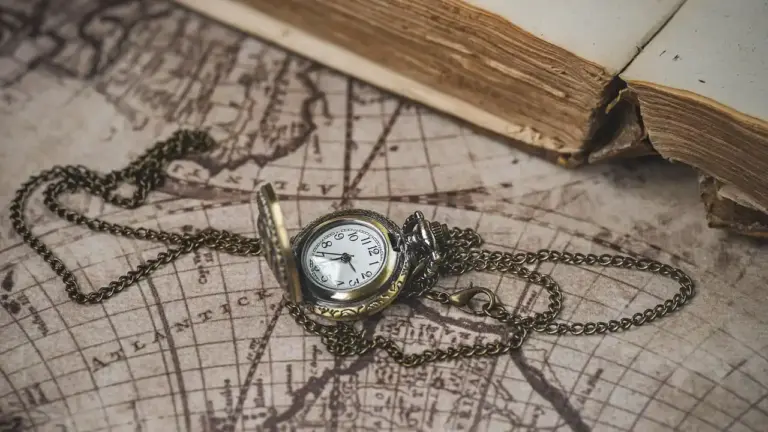 A vintage pocket watch on a brass chain rests on an old map beside the edge of a tattered book, symbolizing time, memory, and survival.