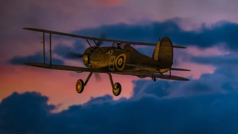 A World War II-era RAF biplane with roundels on its fuselage flying through a sunset sky.