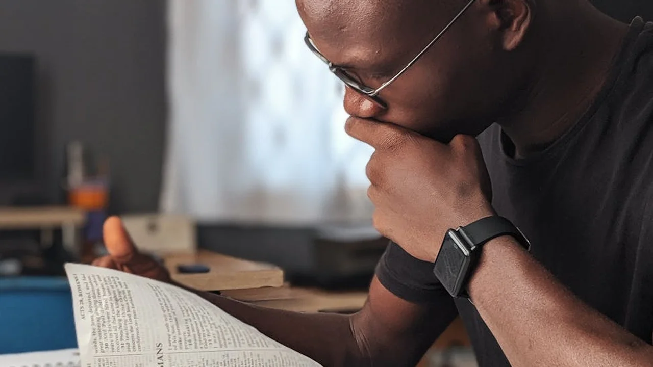 Close-up of a person wearing glasses reading a book, with a thoughtful pose.