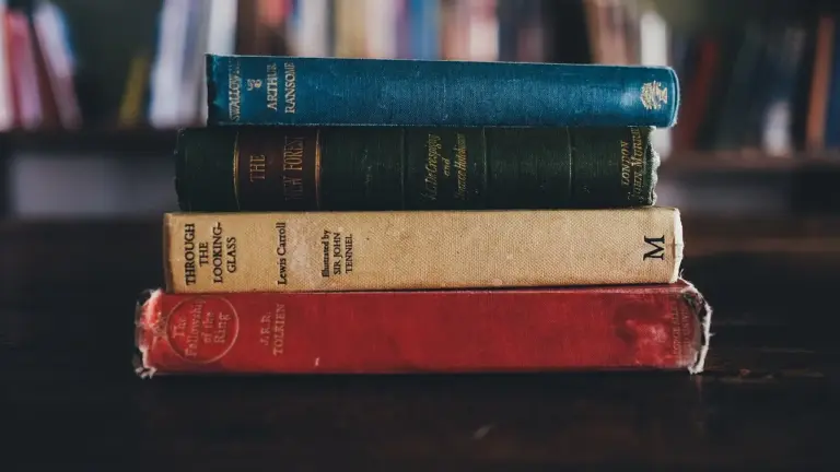 A stack of four vintage hardcover books on a dark wooden surface with a blurred bookshelf in the background.