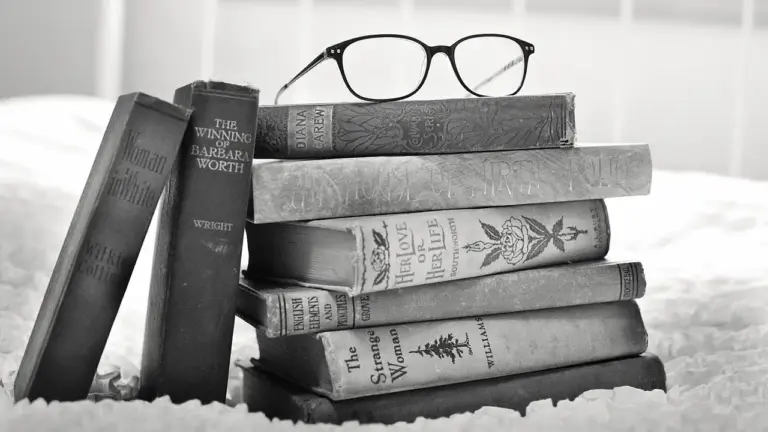 A grayscale photo of a stack of vintage hardcover books with round eyeglasses resting on top, conveying a classic espionage vibe.