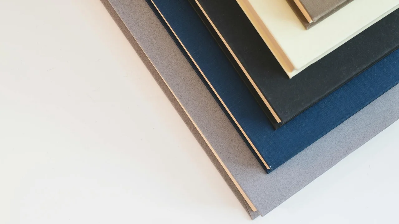 A diagonal stack of hardcover books in various colors resting on a light surface.