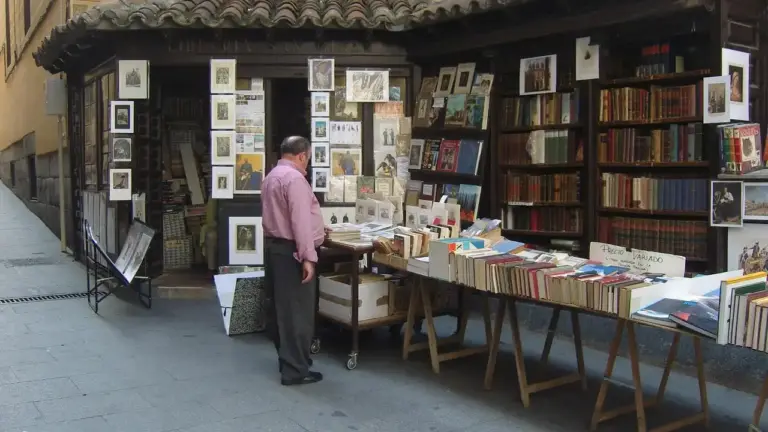 A man in a pink shirt browses a street bookstore filled with books and posters about money and psychology.