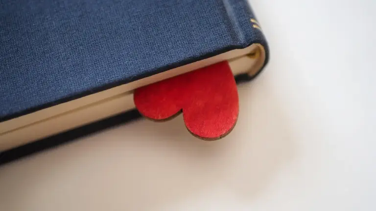 A red heart-shaped bookmark peeking out of a blue hardcover book