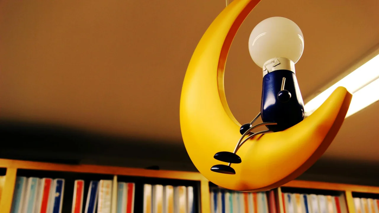 A yellow crescent-moon lamp resting above a row of books on a library shelf.
